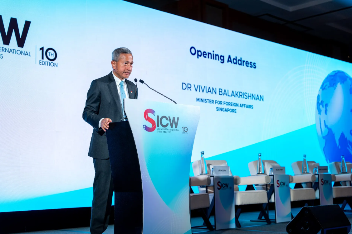 Man at SICW podium giving a speech, large screen behind with globe graphic.